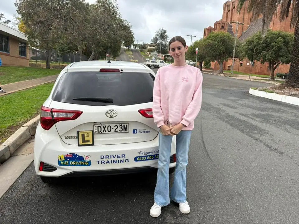 A successful learner has passed her driving test after taking weekend driving lessons with AUZ Driving School and poses proudly with the driving school car